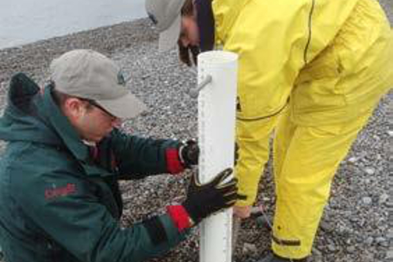 Two people on a beach holding a white sampling tube.