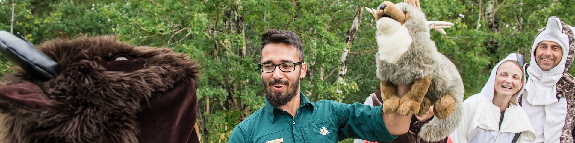 A park interpreter with animal puppets speaks to visitors in animal costumes, Elk Island National Park.