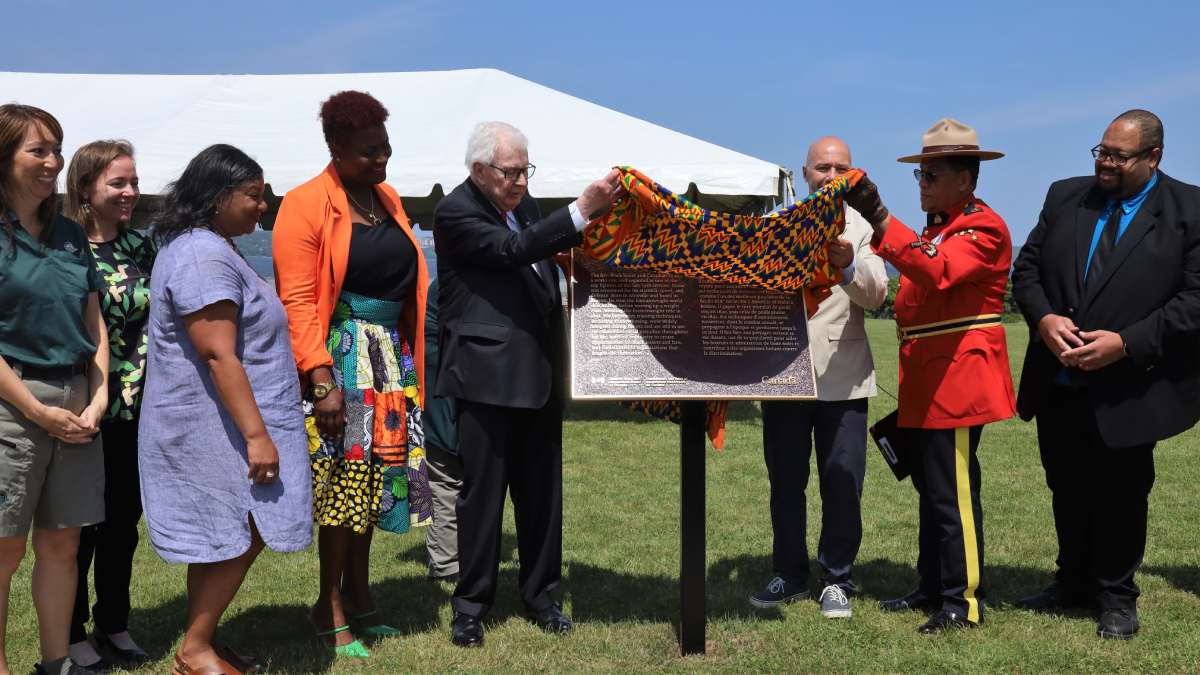 Group of people outdoors unveiling a bronze plaque and blue sky