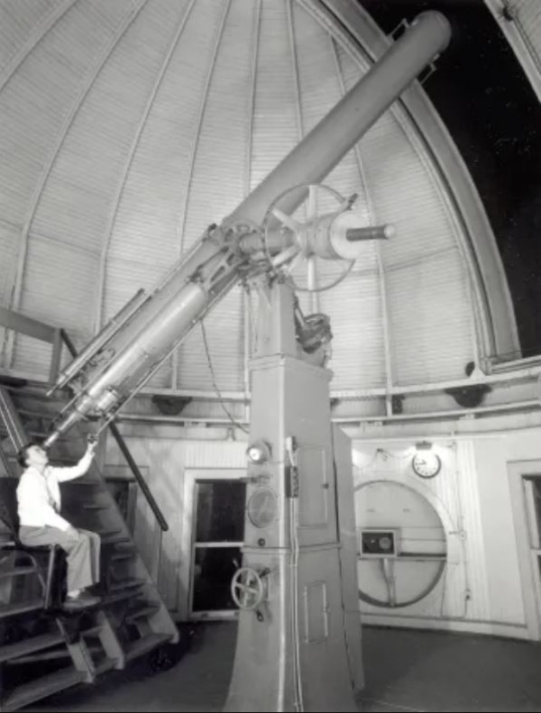 Photo en noir et blanc d'une femme regardant à travers un téléscope dans un observatoire