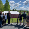 Group of people surrounding a bronze commemorative plaque in a green grass area