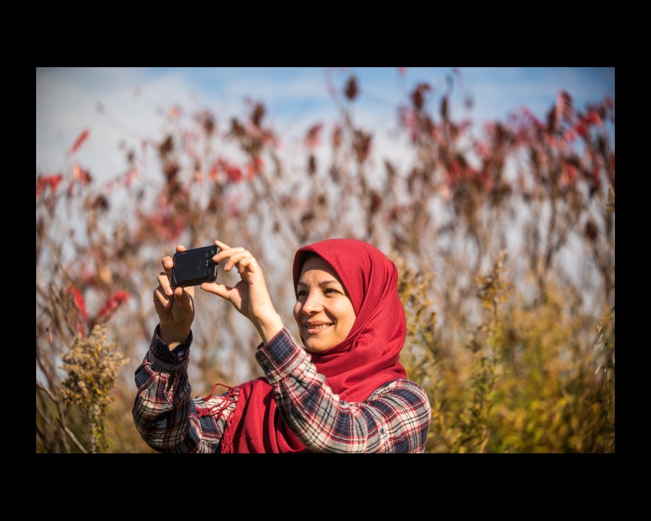 A person smiles while taking a photo among tall grasses.