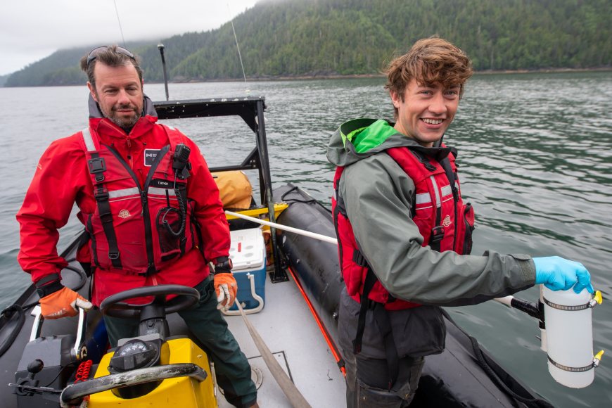 Two researchers working in a boat on the water while collecting a water sample.