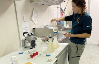 A Parks Canada scientist pours clear solution into a plastic beaker, and filters it through tubes connected to a small vacuum pump.