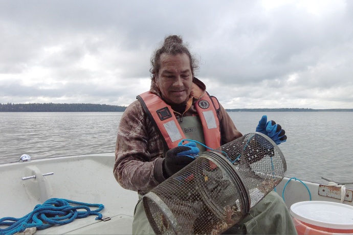 The same person opens a medium sized cylindrical wired trap while in a boat.