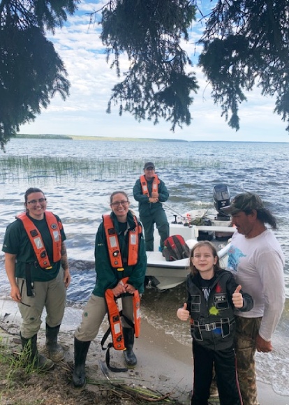 Four adults and one child smile at the camera in front of a boat on the shore.