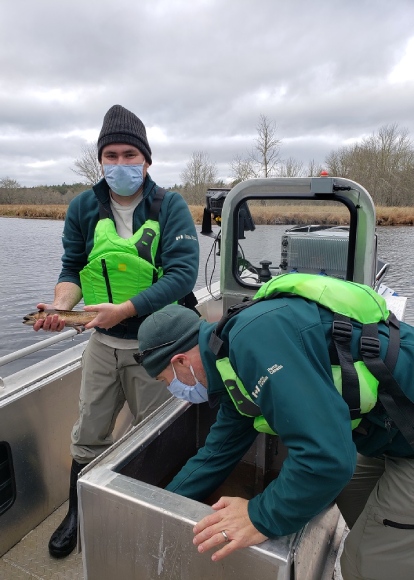 One Parks Canada staff holds a fish while another rummages through a container onboard a boat.