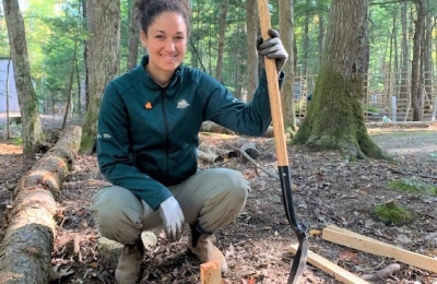 A Parks Canada staff person kneels down with a shovel in hand next to a planted sapling.