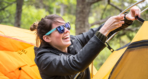 A woman smiles as she sets up a tent.