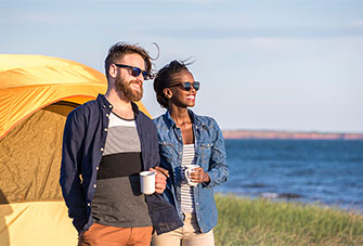 A couple enjoys coffee at sunrise outside their tent, near the water at Cavendish Campground.