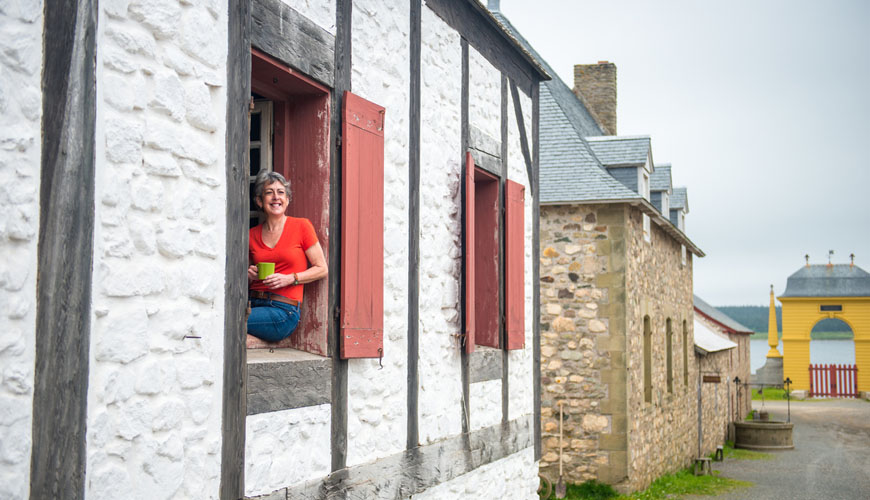 A woman drinks coffee as she sits on the window sill of a period building located in the heart of a fortified town.  