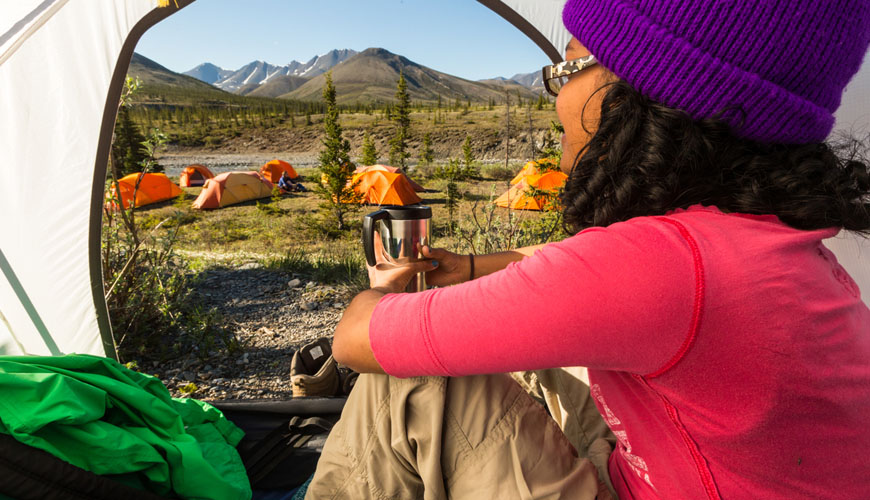 A woman sitting in her tent, looking out at a group of nearby tents.