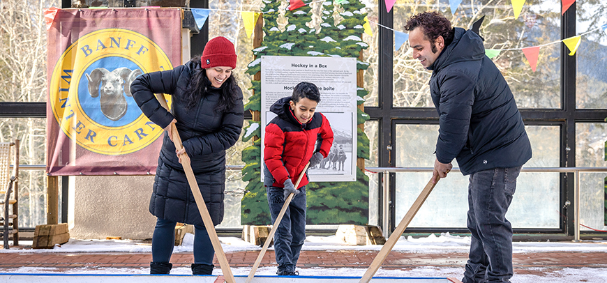 Family playing hockey, moving the puck inside a wood box arena. 