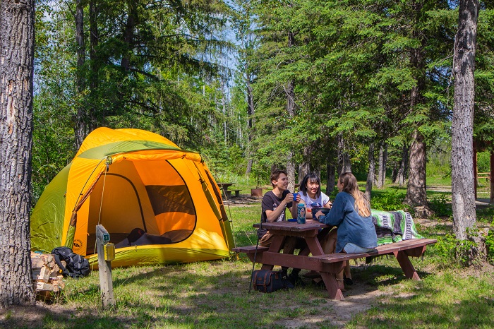 Friends sit at a picnic table in front of their tent