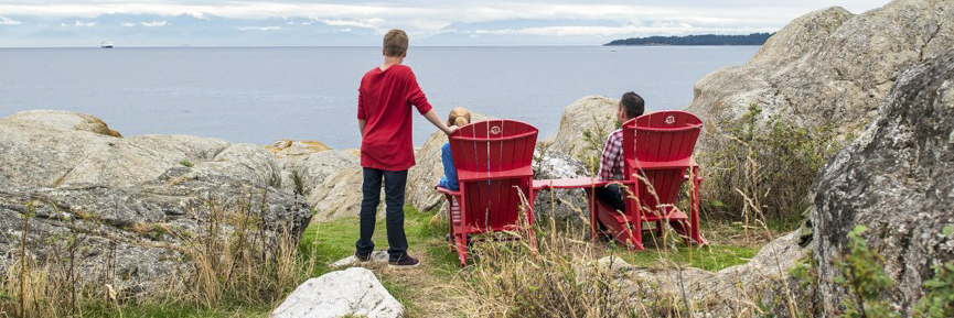 Une mère, avec son fils à ses côtés, et un père sont assis sur les chaises rouges dont la vue porte sur le détroit de Juan de Fuca et la chaine de montagnes Olympic dans l'État de Washington, États-Unis.)