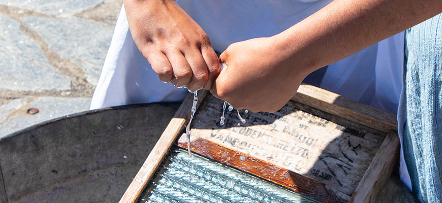 The hands of a person washing laundry with a washboard in a metal basin