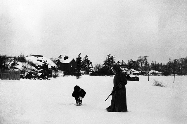 A woman holding a riffle and her young son look for cougar tracks in the snow, circa 1916.