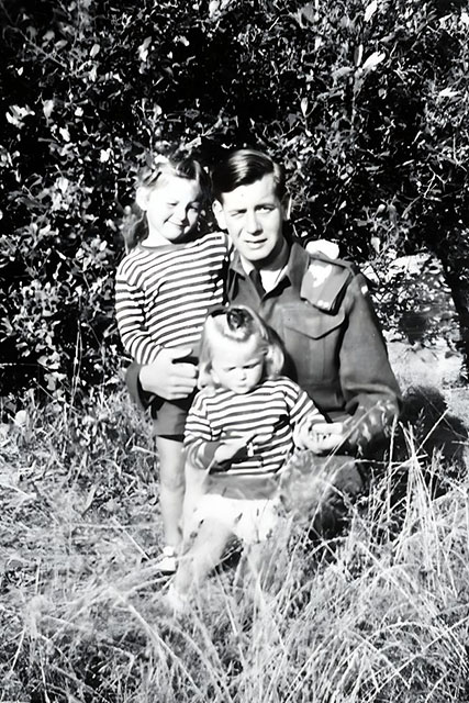 A dad and his three little girls pose in the high grass of the field. 