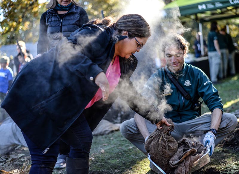 Indigenous knowledge keeper and Parks Canada employee steaming roots in an earthen pit.