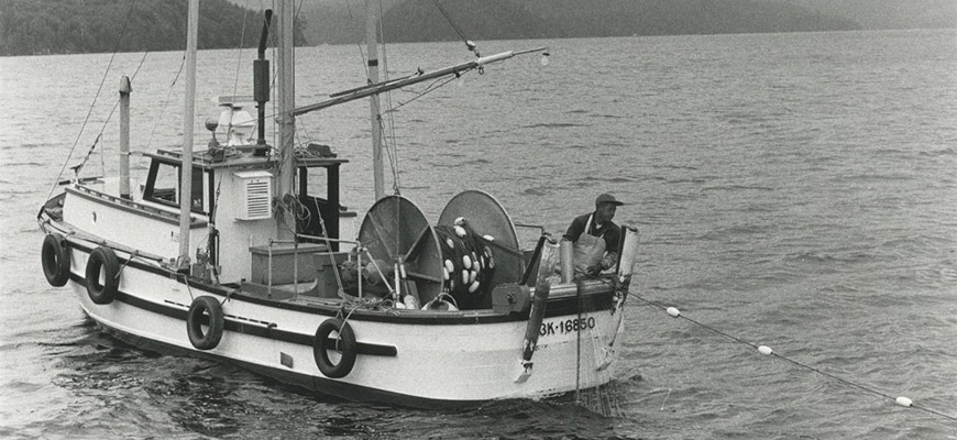 Still frame from vintage black and white film featuring a person fishing from a boat with islands in background