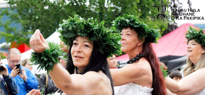 A group of dancers wearing traditional Hawaiian dresses joyfully dance together.