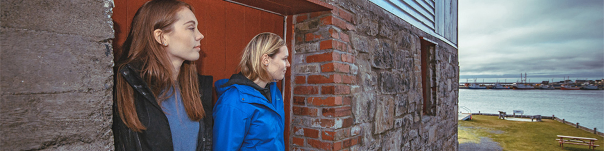 two individuals standing next to a stone structure, looking out over the water