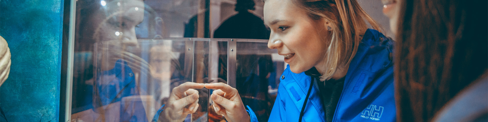 two individuals look closely at a glass exhibit. One is pointing at something in the exhibit.