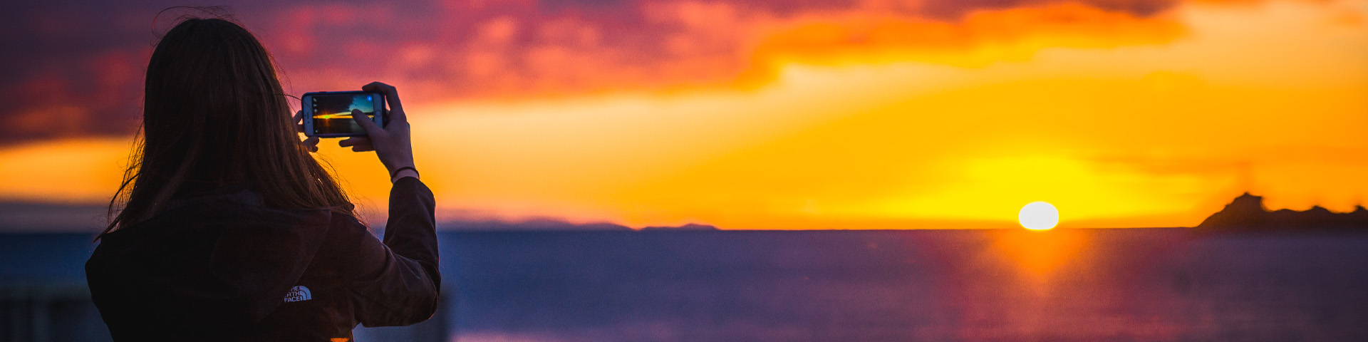 an individual taking a cellphone photo of the sunset 