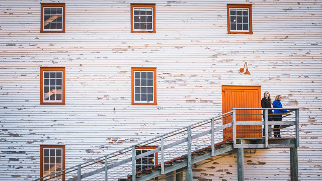 two individuals standing on a wooden staircase next to a white, wooden building