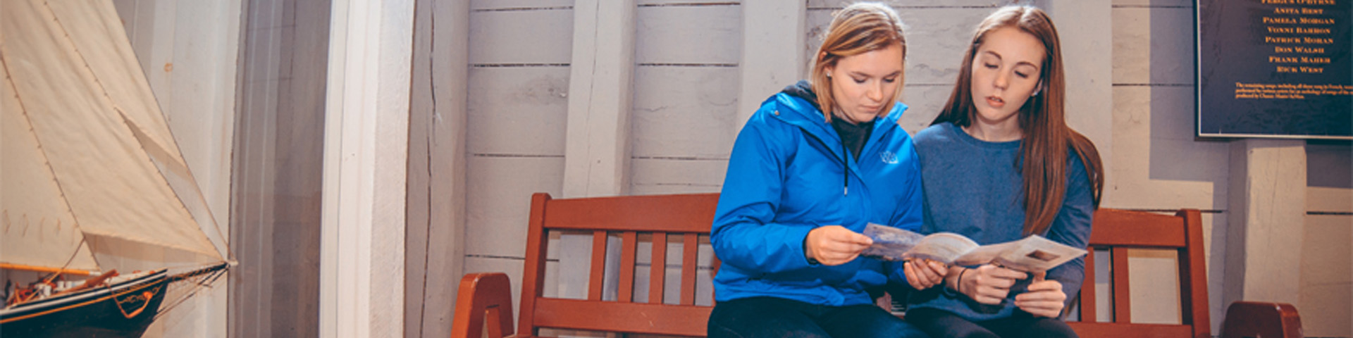 two girls reading a brochure while sitting on a bench