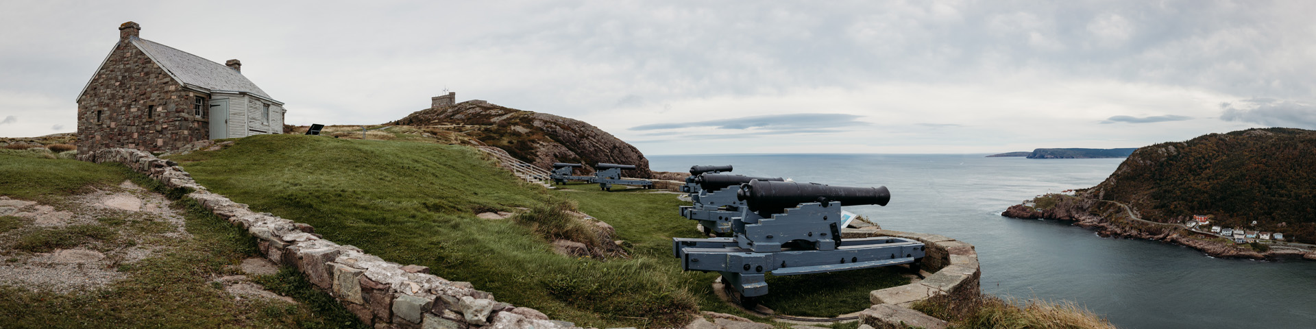 une colline côtière avec des canons historiques et deux bâtiments en pierre. 