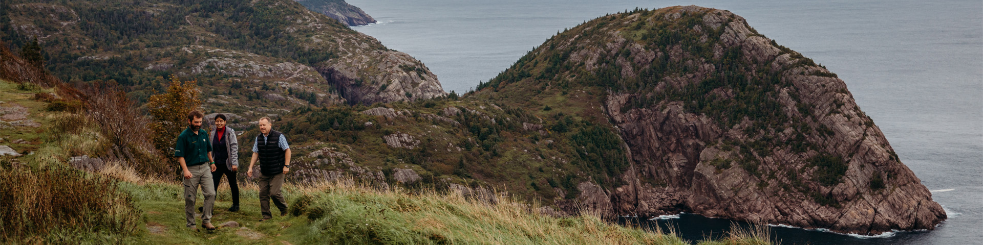 a Parks Canada employee leading two people along a coastal trail