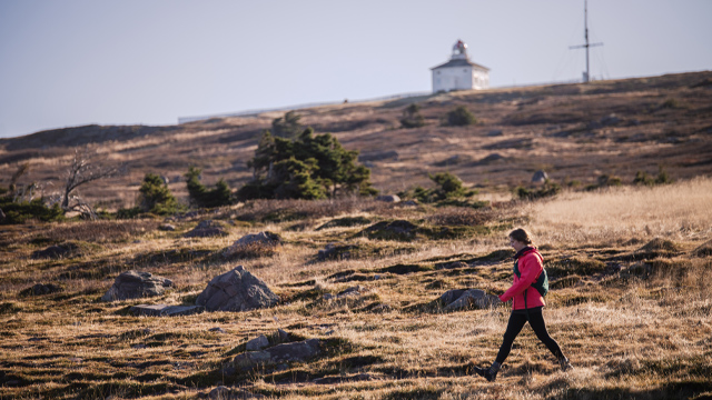 an individual walking along a trail in front of a white, square, wooden building