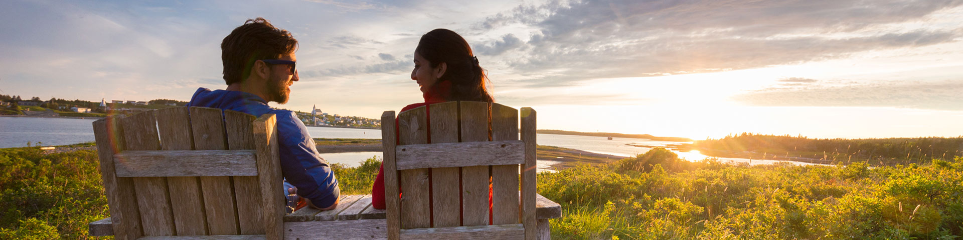 Deux personnes sont assises sur des chaises en bois pendant que le soleil se couche.