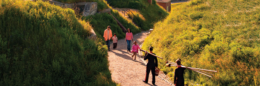 A young family meets costumed interpreters carrying long staffs and buckets of cannon powder along the path at Fort Charlotte.