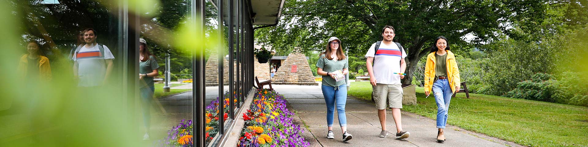 Three people walk on a paved path next to a colourful garden