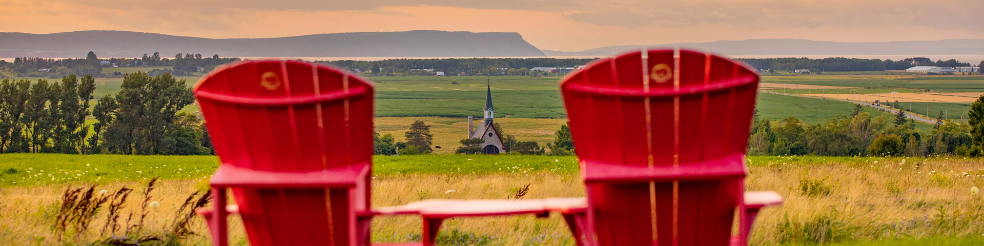 A woman jumping in the air near the red chairs with the Landscape of Grand-Pré in the background