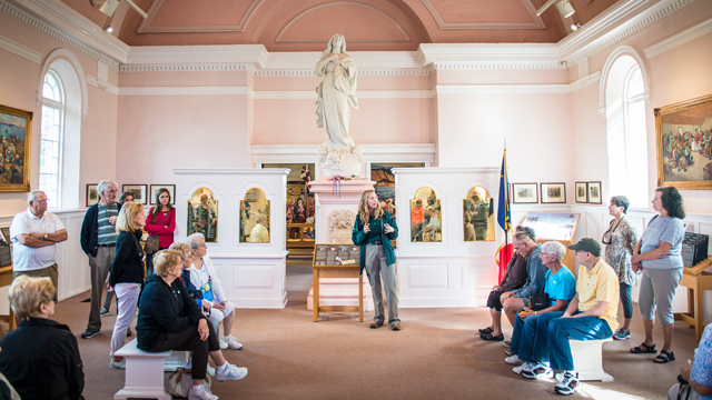 Une interprète de Parcs Canada donne une visite guidée à un groupe de visiteurs à l'intérieur de l'Église-souvenir.