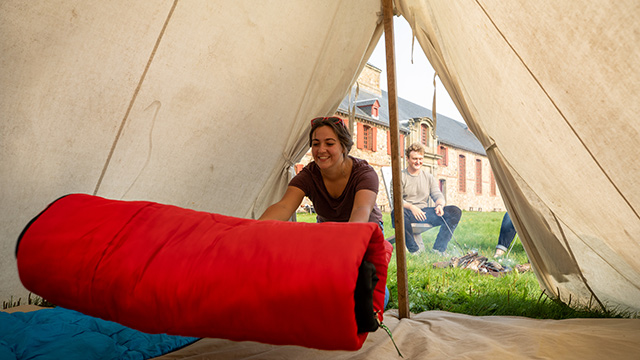 A girl sets up her camping gear in an 18th-century style tent