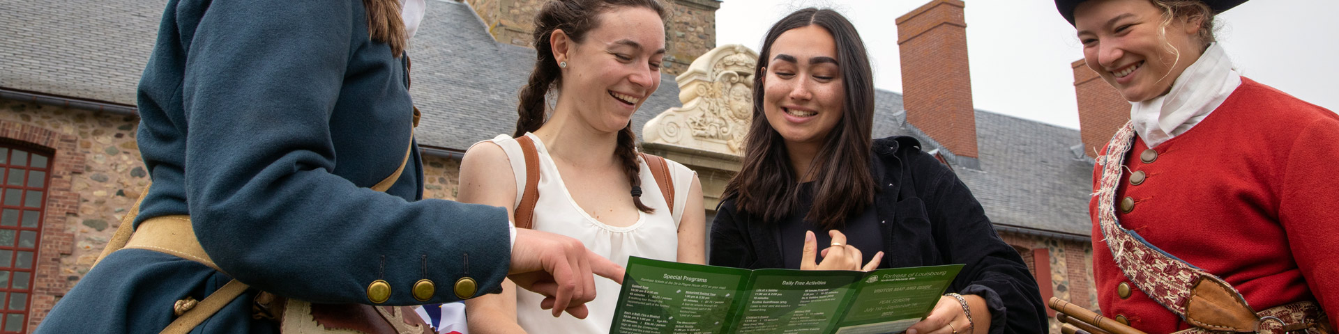 Two visitors look at a brochure with two costumed interpreters