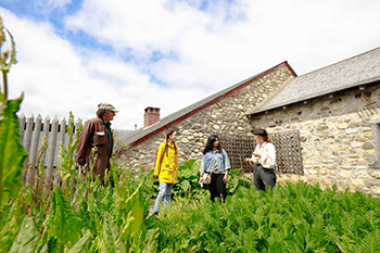 Two visitors stand in a heritage garden speaking with costumed staff