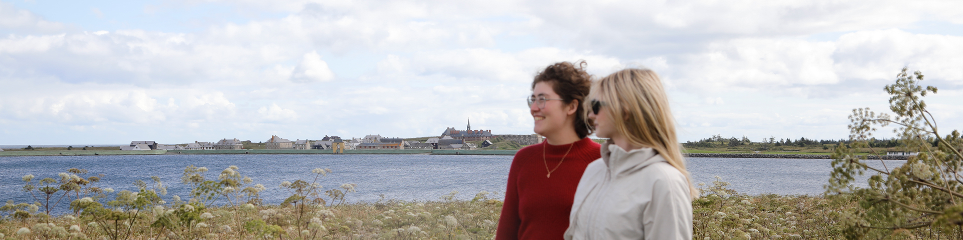 Two people walk along the Old Town Tail with Fortress of Louisbourg National Historic Site in the background.