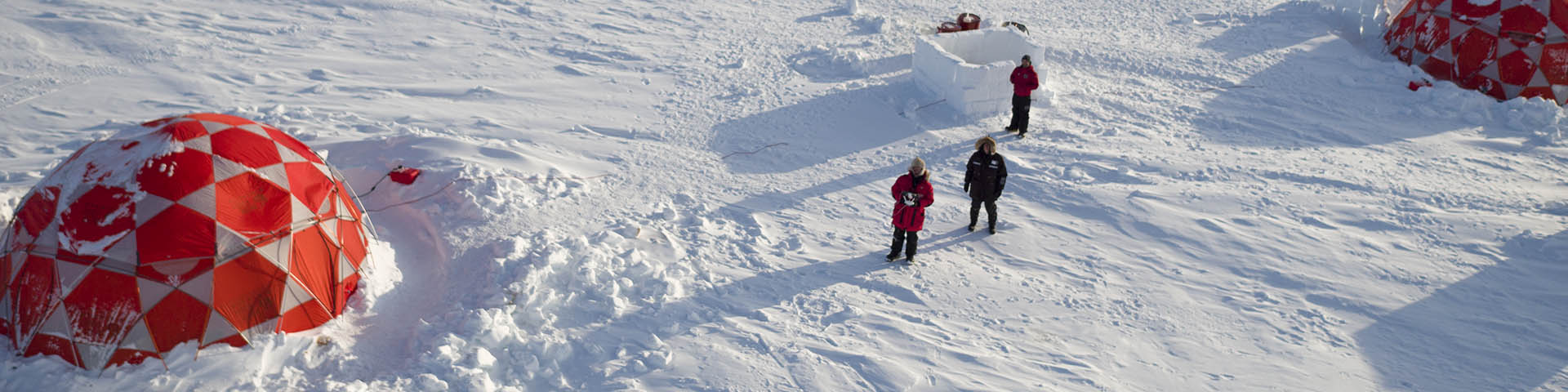 An aerial view of three people standing near tents in the snow. 