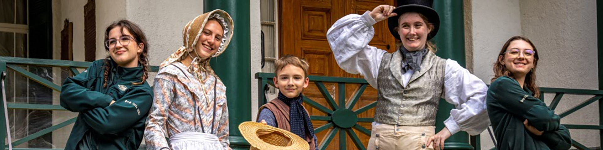 A group in uniforms and costumes stands in front of a historic house. 