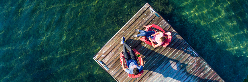 Man and woman on a dock in red chairs.