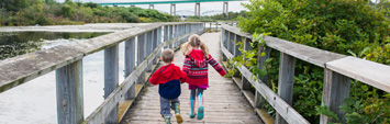 Two children running on a boardwalk.