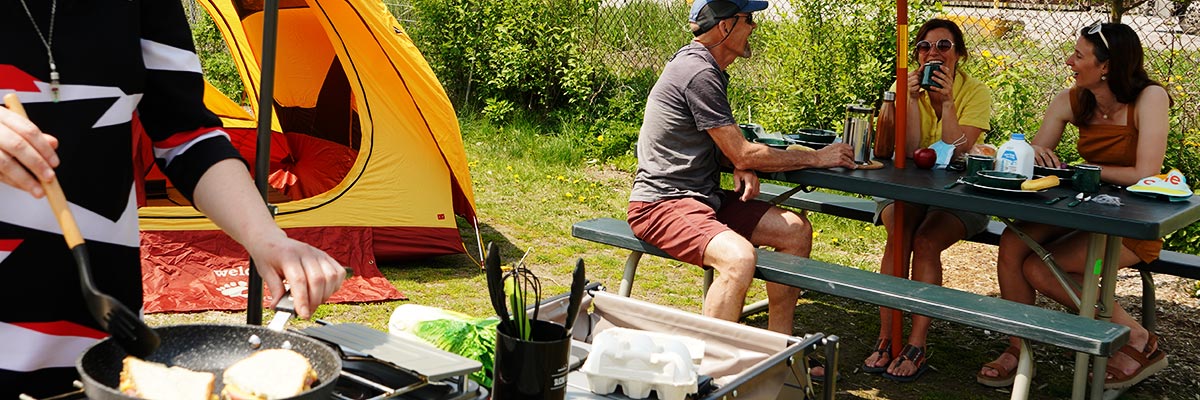 A group of friends enjoying a meal at a campsite on a sunny day. 