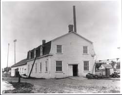 Grand bâtiment avec lucarnes, toit mansard et fenêtres à carreaux servant d'atelier pour le canal de Chambly.