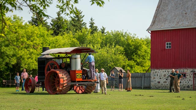 A distance view of a group of people in the barnyard learning about the Hart Parr tractor at Motherwell Homestead NHS.