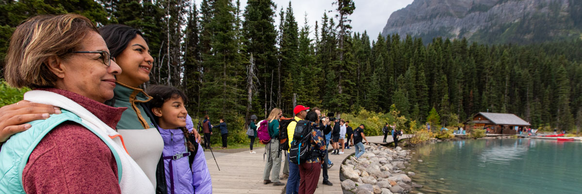 Multiple groups of visitors look out at the view from the Lake Louise Lakeshore with the canoe launch in the background